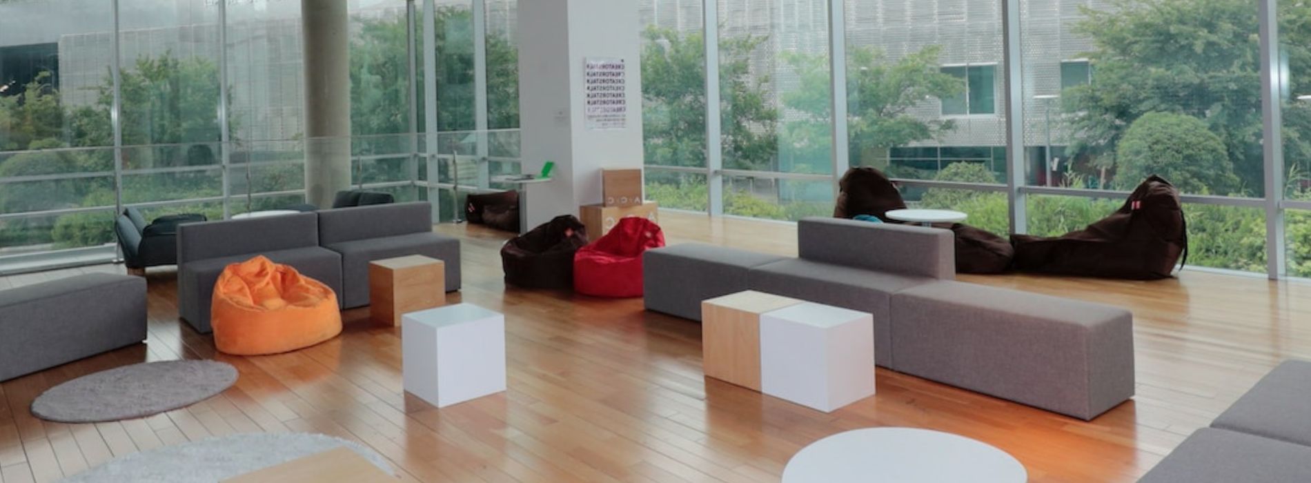A spacious, modern lounge with large windows, hardwood floors, comfortable bean bags, sofas, and minimalist furniture, in a light-filled commercial space in Cheam, SM3.