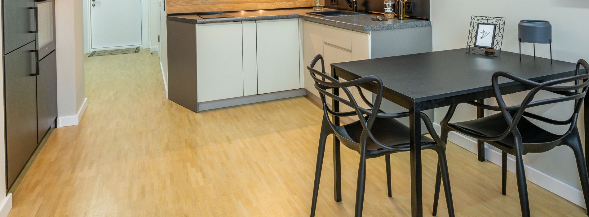 Modern kitchen with light wood flooring, contemporary black dining chairs and table, complemented by professional floor sanding services in South Wimbledon, SW19.