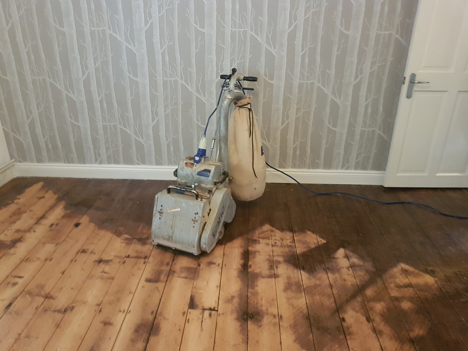 A professional from "Sanding Wood Floors" is using a Bona Belt (AMO110001.3) sander on a floor in Whitchurch, UK. The sander features a 2.2 kW motor, 1-phase power, 200x750 mm or 250x750 mm belt size, drum width of 200 & 250 mm, and a total weight of 74 kg.