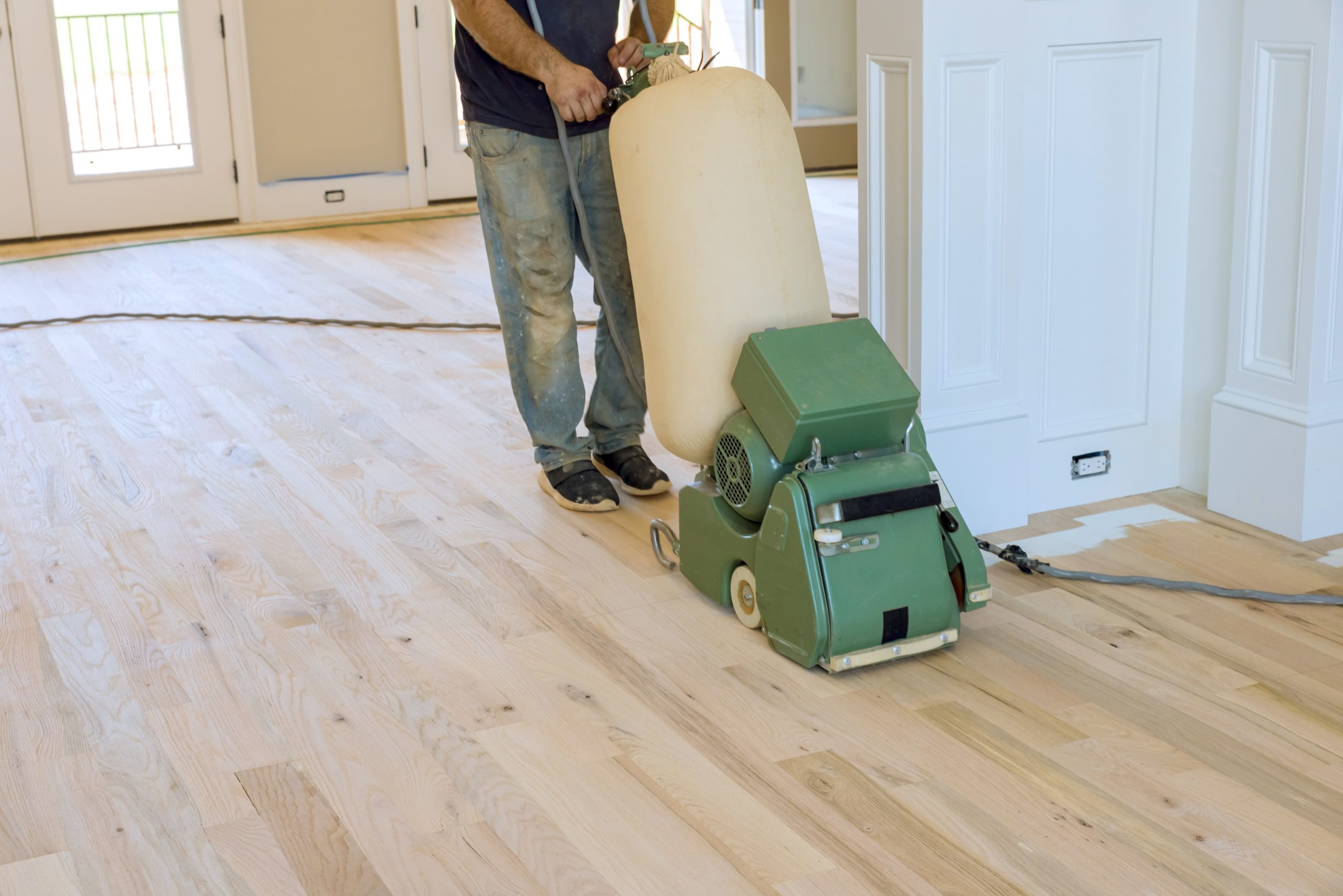 A professional from "Sanding Wood Floors" uses a Lagler HUMMEL&reg; floor sanding machine in Bricket Wood, UK. The HUMMEL&reg; features a 2.2 kW single-phase AC motor, 230 V, 50 Hz, 200 mm drum width, 2400 rpm drum speed, and 200 x 750 mm sanding belt. The machine weighs 79 kg with low dust emissions and adjustable pressure.