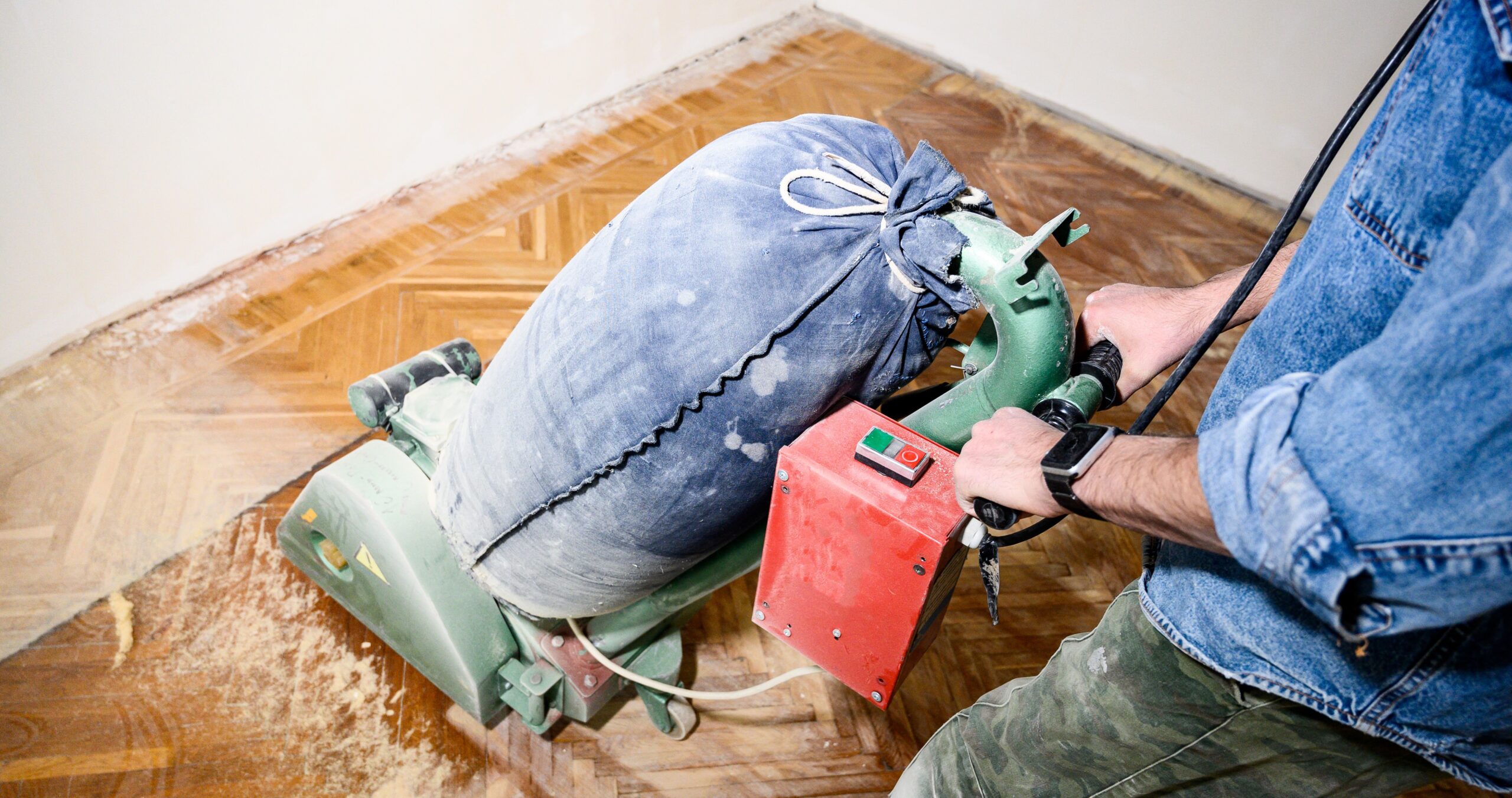 A professional from "Sanding Wood Floors" uses a Lagler HUMMEL&reg; floor sanding machine in Beech, UK. The HUMMEL&reg; features a 2.2 kW single-phase AC motor, 230 V, 50 Hz, 200 mm drum width, 2400 rpm drum speed, and 200 x 750 mm sanding belt. The machine weighs 79 kg with low dust emissions and adjustable pressure.