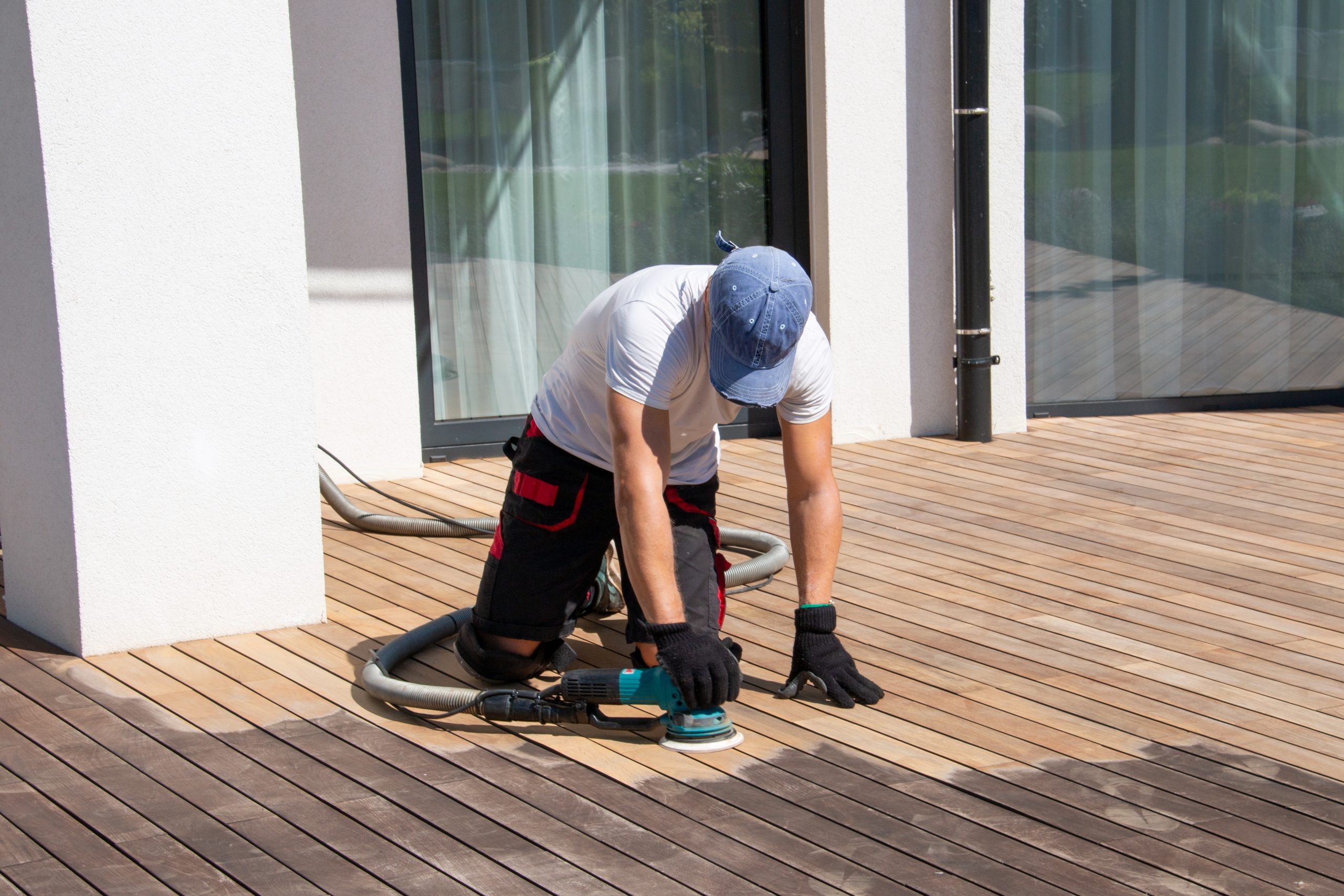 A skilled worker refinishing a wooden deck using a power sander, showcasing the professional floor restoration services provided by "Sanding Wood Floors." The image highlights the attention to detail and craftsmanship in transforming worn wood surfaces into pristine finishes.