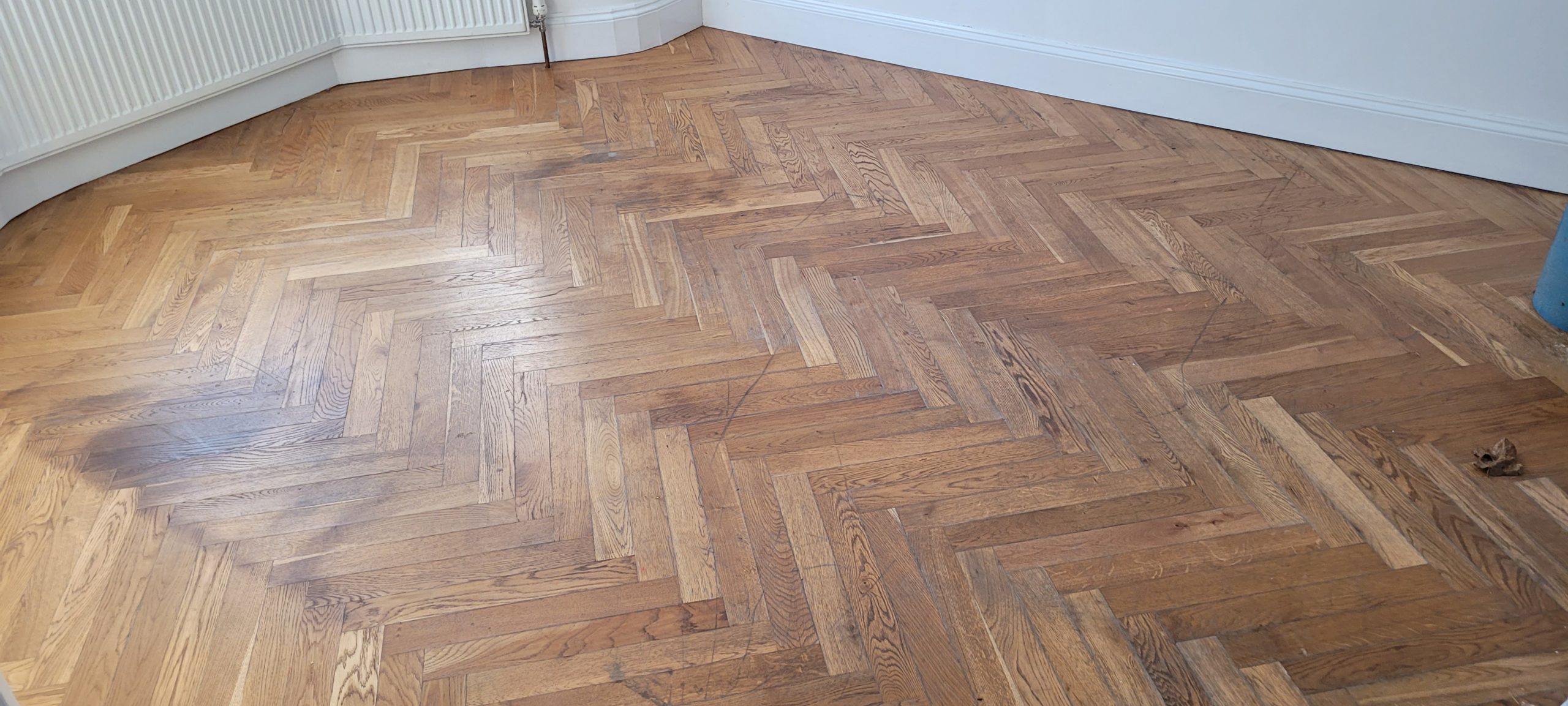 Worn oak herringbone parquet wood floor needing work, captured before reviving painted floorboards begins.