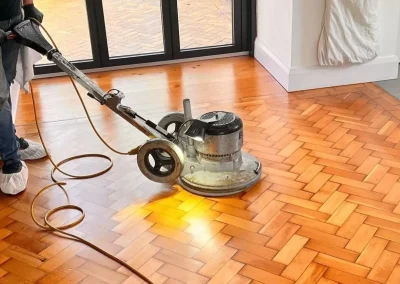 Buffer vs Polisher: professional using a low-speed rotary buffer on an oak herringbone parquet wood floor, preparing the surface for recoating and final polish.