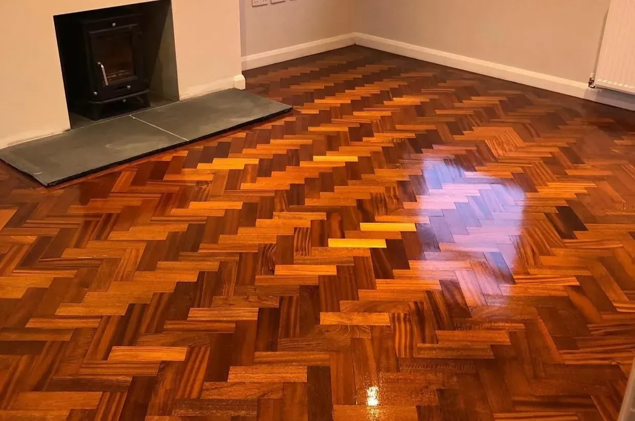 Parquet Repairs — freshly restored oak herringbone parquet floor (wood block parquet type) with rich stain and high-gloss lacquer, seamless finish around fireplace.