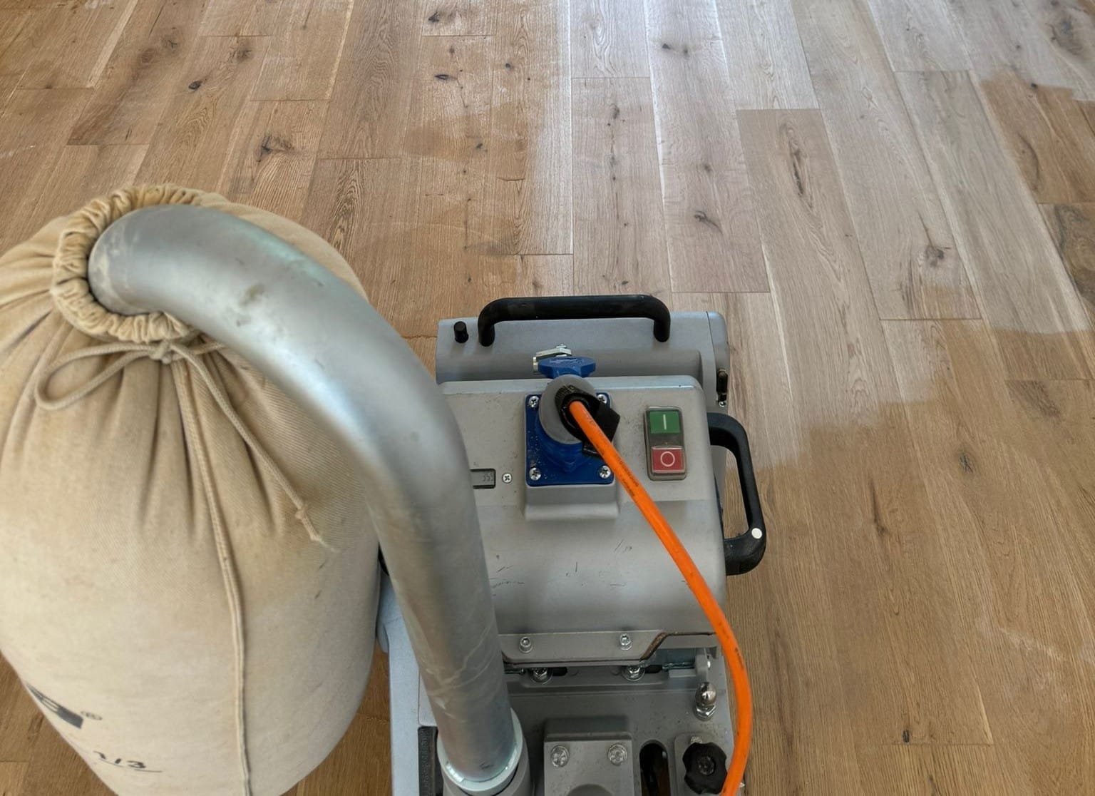 Office Floor Sanding close-up on solid oak plank hardwood floor with a dust-extracted belt sander midway through the first pass.
