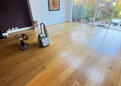 How to Fix Dull Traffic Lanes on an oak engineered living room floor, with sanding machines ready to restore the worn, pale traffic areas near the windows.